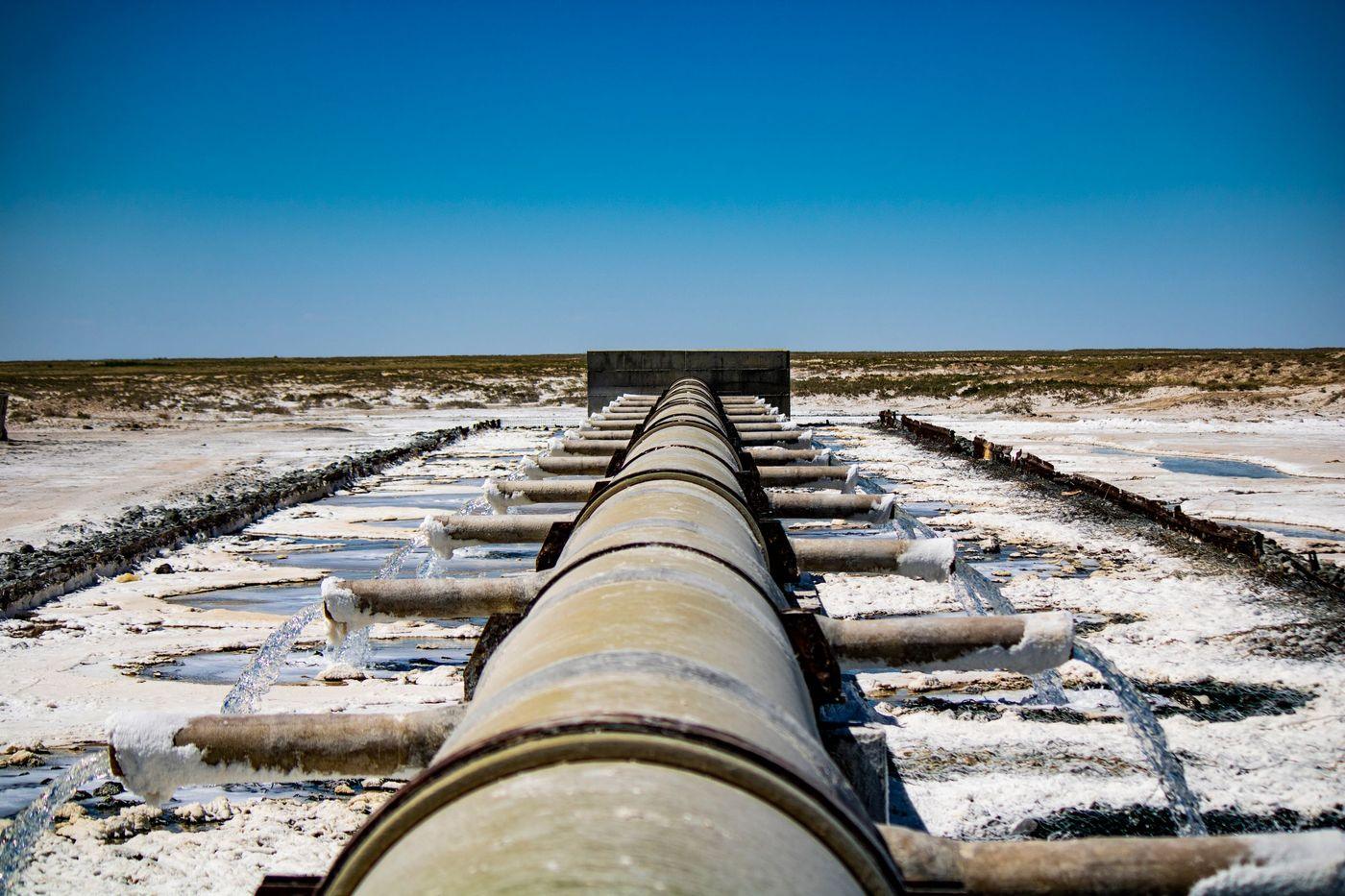 An industrial pipeline discharging water across dry, arid ground
