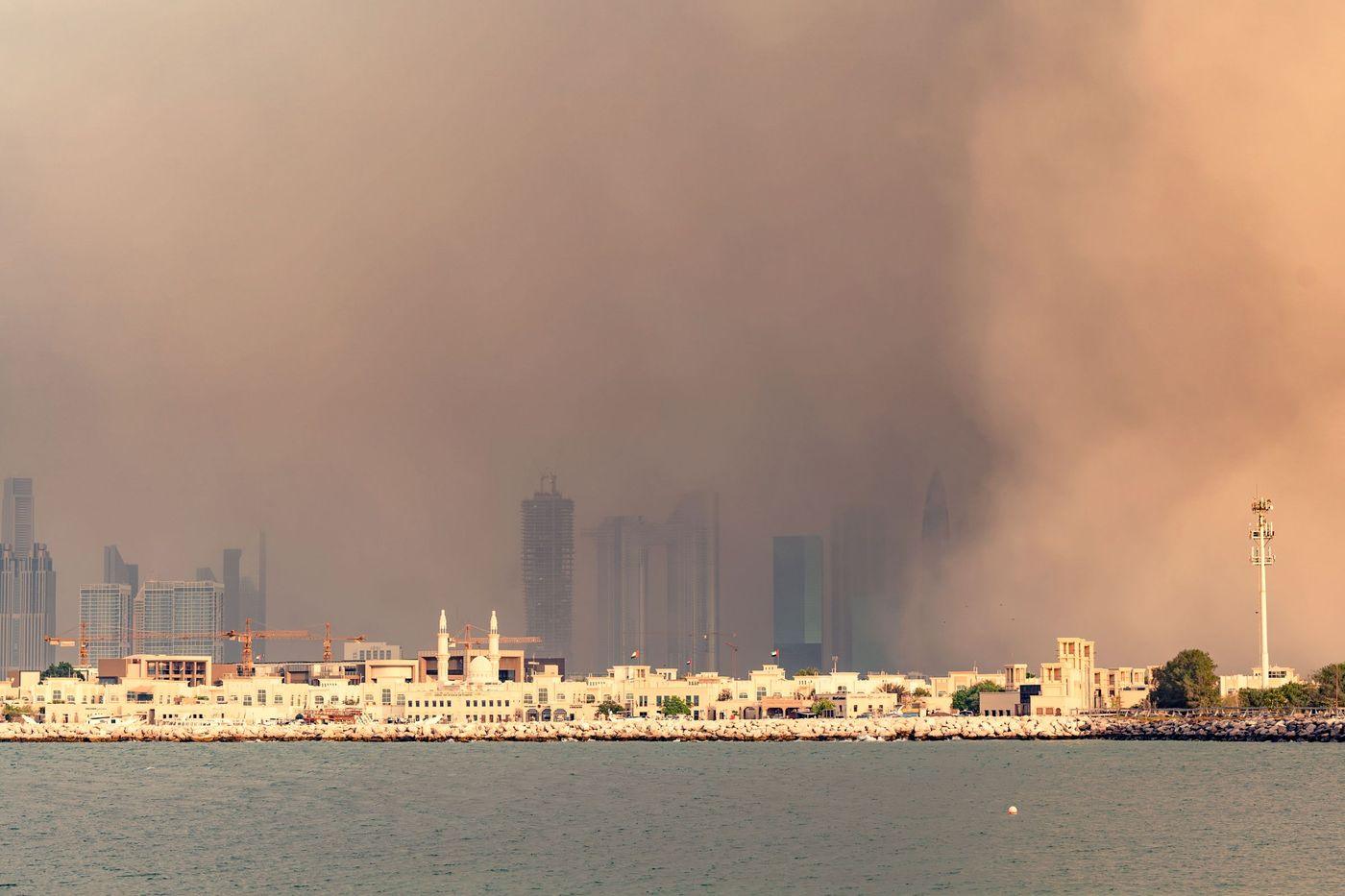 A dense sandstorm rolling in over a Gulf city skyline, seen from across the water