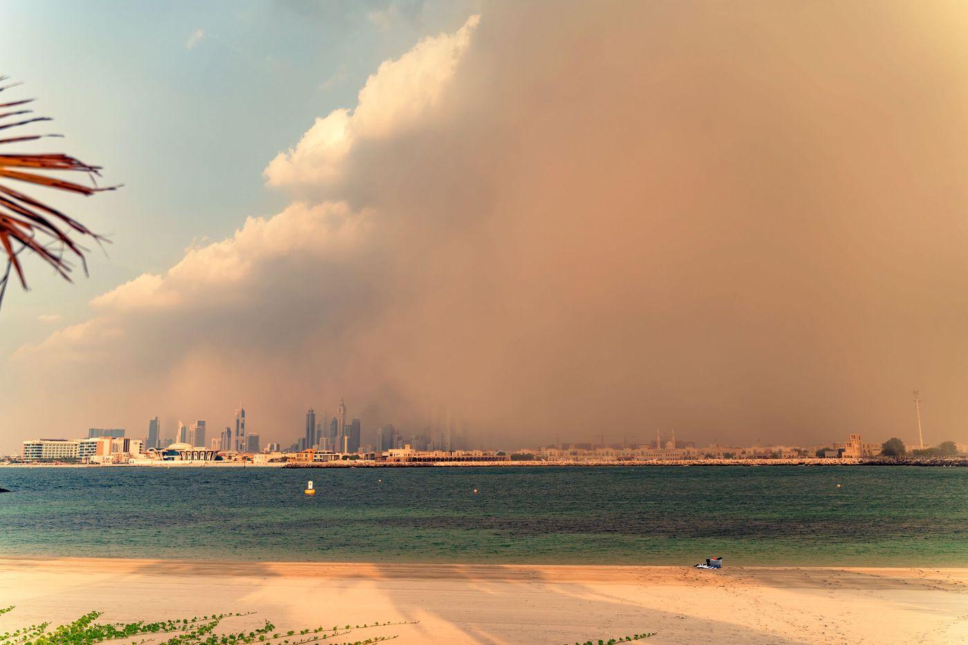 A wall of dust approaching a coastal skyline while the sea in front of it stays calm